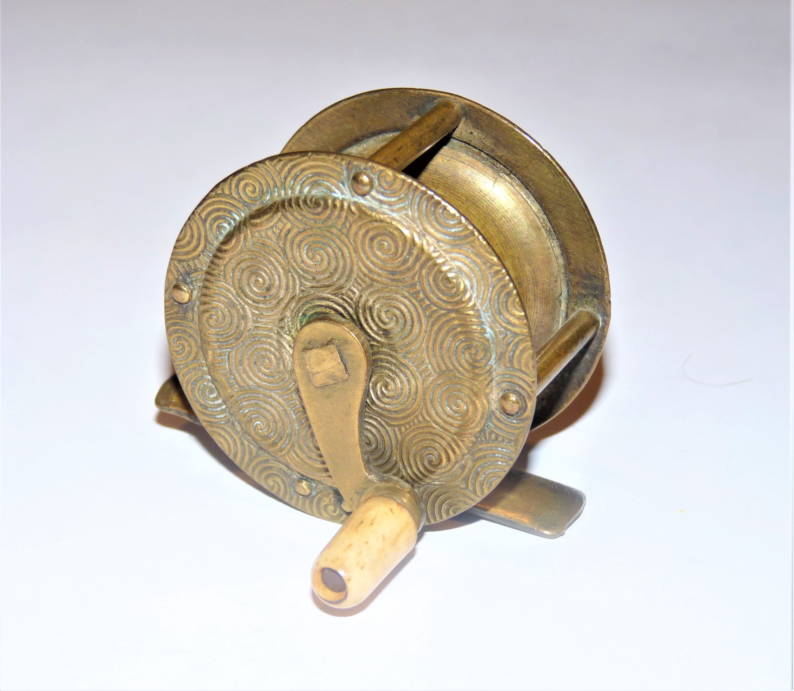 Brass 2" vintage fishing reel with decorative flower swirl to front & back plates to display