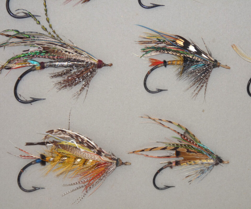 Alternative view of 14 antique large gut eyed salmon flies stitched onto grey card, hook sizes 1/0 to 7/0